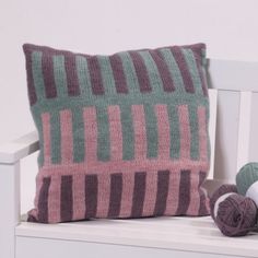 a knitted pillow sitting on top of a white bench next to a ball of yarn