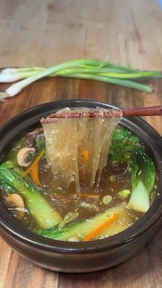 a bowl filled with soup and vegetables on top of a wooden table next to chopsticks