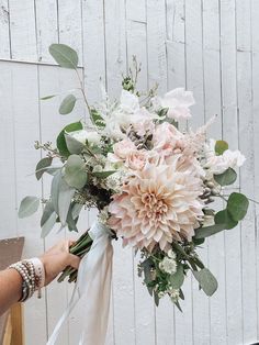 a bouquet of flowers is being held up by someone's hand with a white ribbon