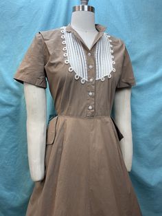 "1940s/1950s W:32 Vintage 40s 50s taupe brown shirt dress white big side pockets short sleeve  Great 40s/50s dress in light brown, taupe color. Button up shirt with shank pearls with short sleeve and white contrast bib trim with fagoting stitch. Side pockets. Side zipper. Beautiful vintage off white dress made of light weight nylon with seersucker embossing. Side zipper.  Photographed on fitting form size 8, check measurements.  MEASUREMENTS  Bust: 40\" Waist: 32\" Hips: free\" Bodice length: 17 1/2\" Skirt Length: 30\" with no hem available This is in good vintage condition, small 0.25\" hole in the back bodice near seam, some stress to seam and loose buttons. Sold as is  ✨" 1940 Shirt Women, 1940s Inspired Fashion, 1950s Style Vintage Dress With Button Closure, 40s Dresses, Toothpaste Kisses, 1950s Short Sleeve Cotton Dress, Dracula Film, 1950 Shirtdress, Beth Harmon