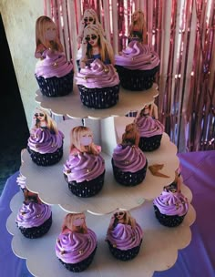 cupcakes with purple frosting and barbie dolls on top are arranged in a tiered display