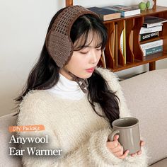 a woman sitting on a couch holding a coffee cup in her right hand and wearing a knitted headband