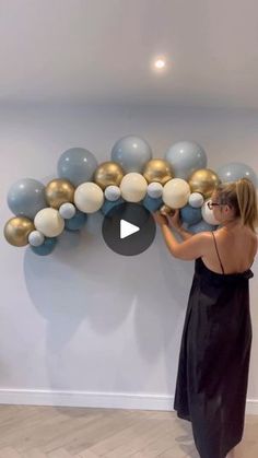 a woman in a black dress is painting balloons on the wall with gold and silver balls