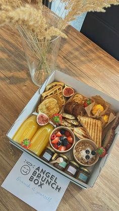 an open lunch box sitting on top of a wooden table next to a vase filled with flowers