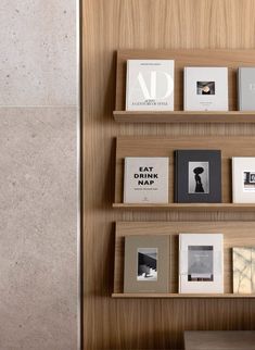 several books are arranged on wooden shelves in front of a wall with marble tiles and wood paneling