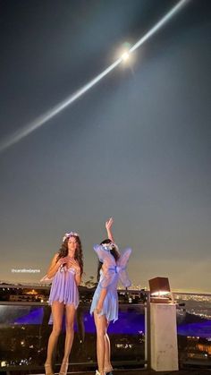 two women standing on top of a roof with an airplane in the sky behind them