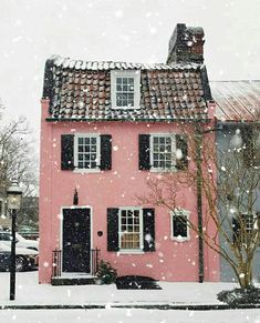 a pink house with black shutters and snow falling on the ground in front of it