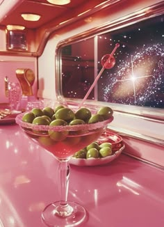 a pink counter with green olives in a martini glass on it next to a window