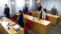 a group of people in suits and ties standing around desks with microphones on them