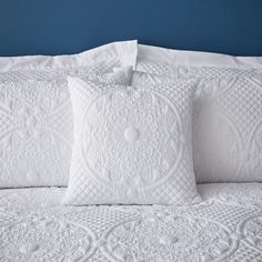 three white pillows sitting on top of a bed next to each other in front of a blue wall