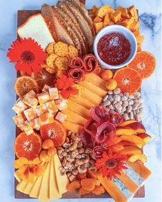 an assortment of cheeses, crackers and fruit on a cutting board with flowers