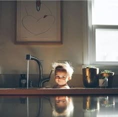 a young child is sitting in the sink with his reflection on the counter top and looking at the camera