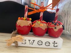 three apples with candy toppings on them sitting in front of a sign that says sweet