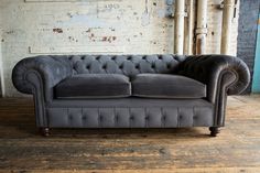 a grey couch sitting on top of a wooden floor next to a white brick wall