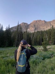 a woman with long blonde hair wearing a blue backpack is looking through binoculars at the mountains