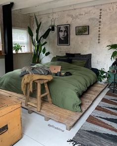 a bed with green sheets and pillows in a bedroom next to a wooden trunk on the floor