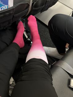 a person with pink socks and black pants sitting on an airplane seat next to luggage