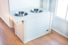 two stainless steel bowls sit on top of a white dog house that is built into the floor