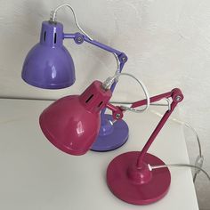 two pink and purple desk lamps sitting on top of a white table next to each other