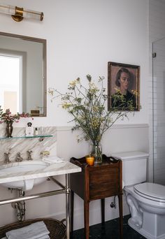 a bathroom with a sink, toilet and painting on the wall above it's mirror