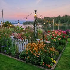 a garden filled with lots of flowers next to a white fence and light poles in the background