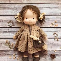 a little doll with brown hair and dress holding a teddy bear in her hand on a wooden floor