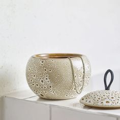 a white vase sitting on top of a counter next to a ceramic bowl with a black handle