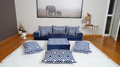 a living room with blue and white pillows on the floor, an elephant in the background