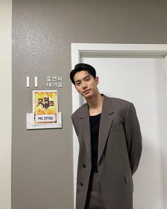 a man standing in front of a door wearing a gray suit and black t - shirt