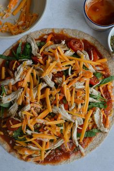 a pizza topped with cheese and spinach on top of a white table next to bowls of sauce