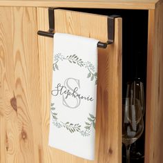 a towel hanging on a wooden cabinet with wine glasses in the bottom drawer and a personalized monogrammed dish towel