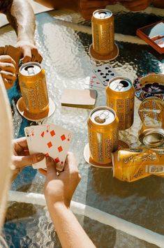 two people playing cards at a table with beer cans on it and other items around the table