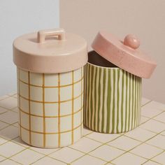 two ceramic containers sitting on top of a tiled counter next to each other, one with a lid and the other with a handle