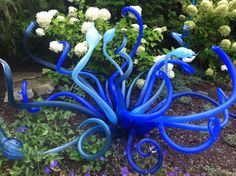 a blue sculpture in the middle of some flowers