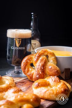 some pretzels on a cutting board next to a glass of beer