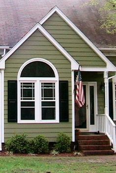 a green house with an american flag on the front door and steps leading up to it