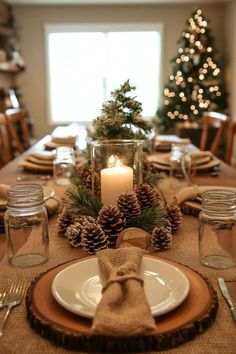 a table set for christmas with pine cones, candles and napkins on the place setting