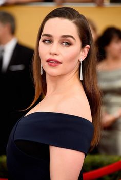 a woman in a black dress with long hair and earrings on the red carpet at an event