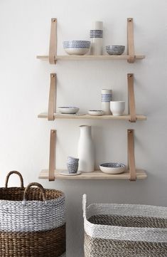 two shelves with bowls and cups on them in front of a wall mounted shelf filled with wicker baskets