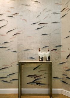 a wall with fish painted on it and a vase sitting on top of the table