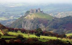 a castle on top of a hill surrounded by lush green hills and trees in the foreground