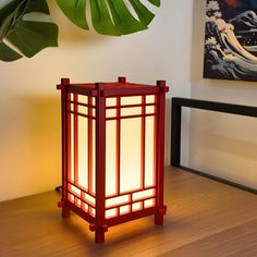 a red lantern sitting on top of a wooden table next to a green leafy plant