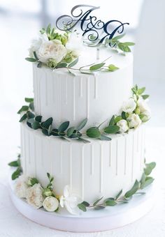 a three tiered white wedding cake with greenery and monograms on top