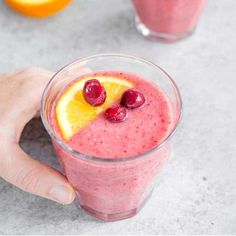 a person holding a glass with a fruit smoothie in it and garnished with cherries