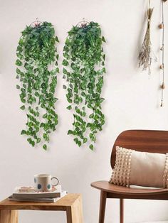 two green plants hanging from the side of a white wall next to a wooden chair