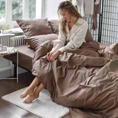 a woman sitting on top of a bed covered in brown sheets