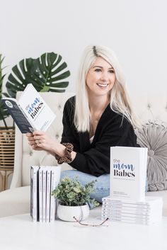 a woman sitting on a couch holding a book in front of some books and plants