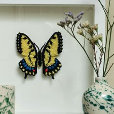 a yellow and black butterfly sitting on top of a white frame next to some flowers