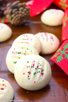 white cookies with colorful sprinkles are on a table next to pine cones