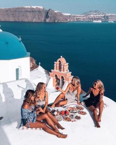 three women sitting on the edge of a cliff with plates of food in front of them